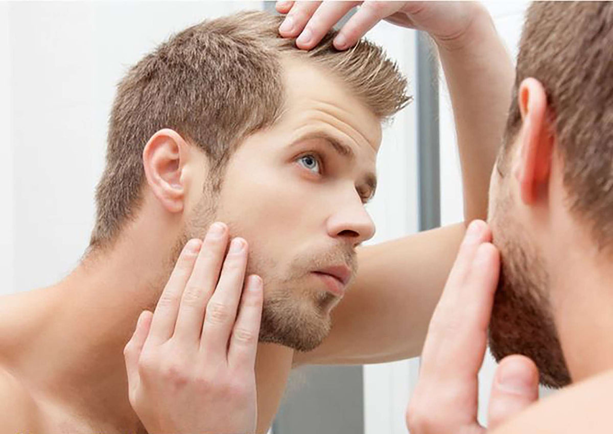 man examining thinning hair in mirror using NORMADENSE 2 Prowash vegan shampoo for denser hair